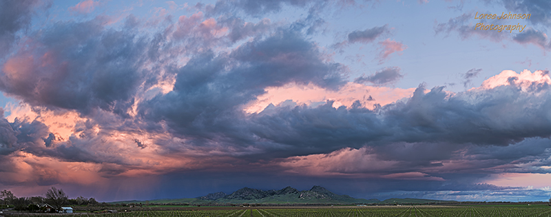 A thunderstorm rolls in over the Sutter Buttes in the central valley of California at sunset. In this view from the west,the swirling clouds are illuminated by the setting sun in a dramatic weather display.